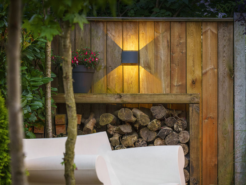 Leuchte Goura an Holzwand vor Terrassenstuhl