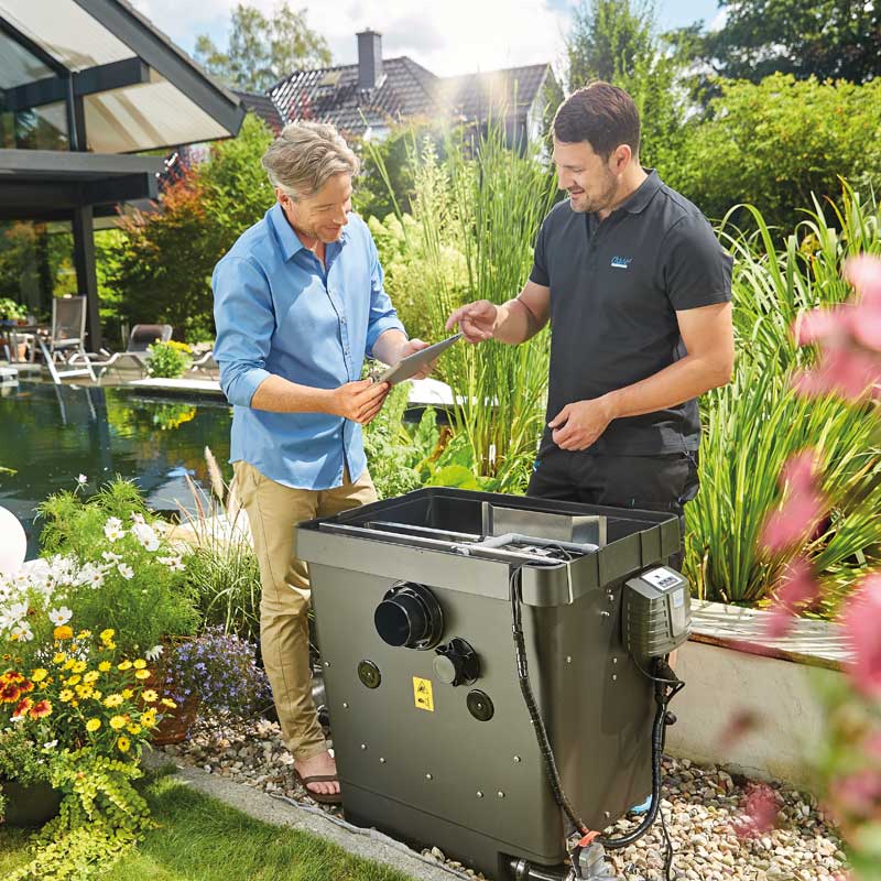 Zwei Maenner stehen neben einem Teichfilter