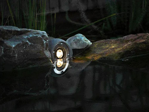 Spotstrahler Lapis steht am Teichrand und beleuchtet die Wasseroberflaeche