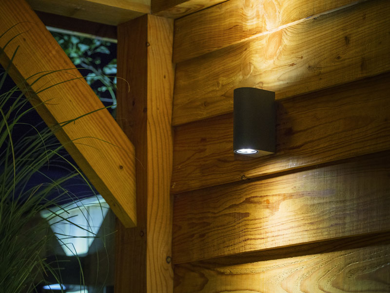 Wandleuchte Sibus beleuchtet eine Holzwand bei Nacht
